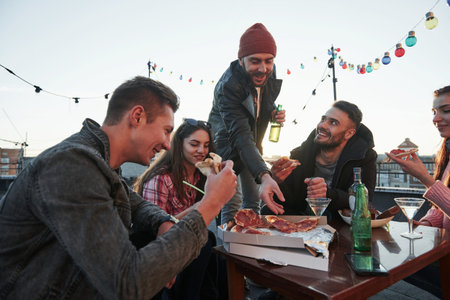 Give him one more slice. Eating pizza at the rooftop party. Good friends have weekend with some...