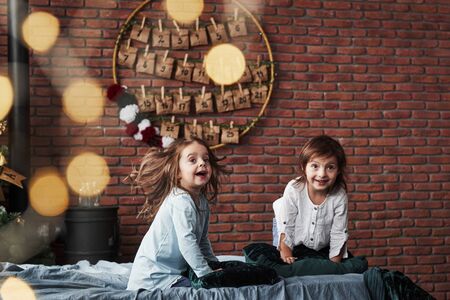 Carefree smiles. Little girls having fun on the bed with holiday interior at the background.の写真素材