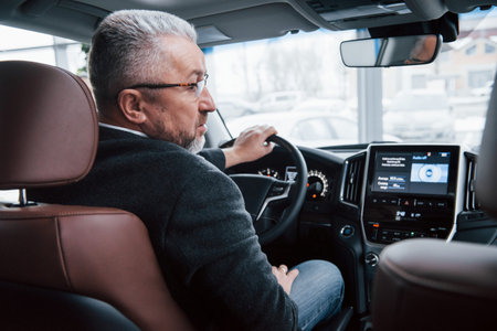 Ready to the ride. View from behind of senior businessman in official clothes driving a modern new...