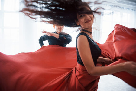 Photo of motion. Young pretty woman in red and black clothes dancing with bald guy in the white...