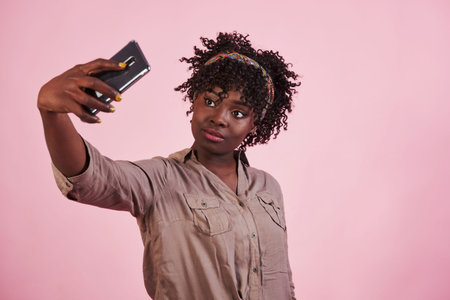 Yellow painted fingernails. Attractive afro american woman in casual clothes takes selfie at pink...