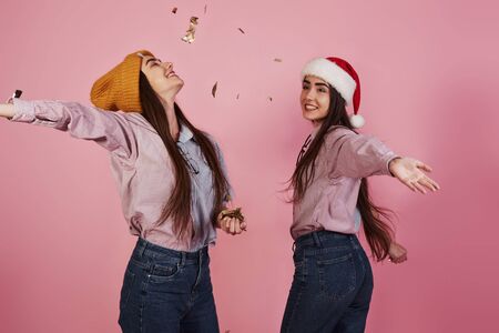 New year conception. Two twins playing throwing golden confetti in the air in the studio with pink background.の写真素材