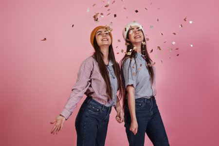 Holiday mood. New year conception. Two twins playing throwing golden confetti in the air in the...