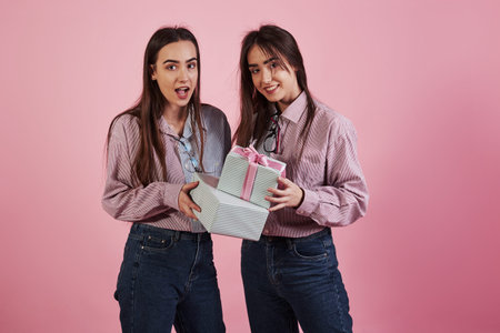 Gives you holiday presents. Young women having fun in the studio with pink background. Adorable twins.の写真素材