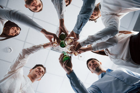 Photo from below. Knocking glasses in the office. Celebrating success.