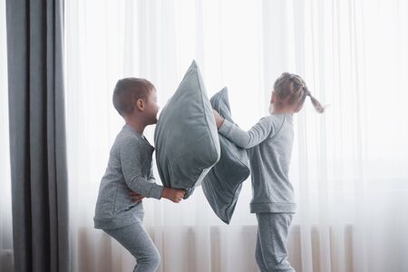 Little boy and girl staged a pillow fight on the bed in the bedroom. Naughty children beat each other pillows. They like that kind of game.の写真素材