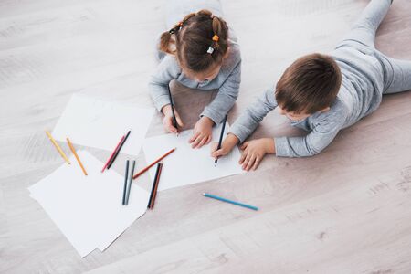 Children lie on the floor in pajamas and draw with pencils. Cute child painting by pencils.の写真素材