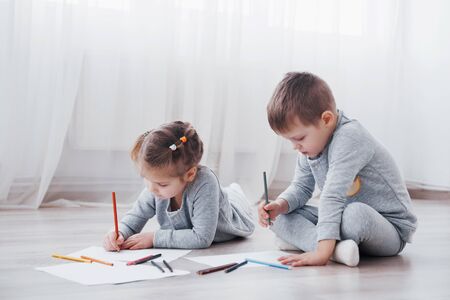 Children lie on the floor in pajamas and draw with pencils. Cute child painting by pencils.の写真素材
