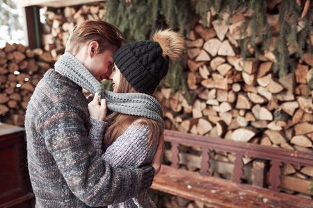 winter, vacation, couple, christmas and people concept - smiling man and woman in hats and scarf hugging over wooden country house and snow background.の写真素材