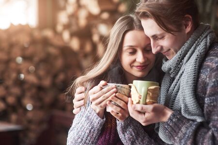 Young couple having breakfast in a romantic cabin outdoors in winter. Winter holiday and vacation. Christmas couple of happy man and woman drink hot wine. Couple in love.の写真素材