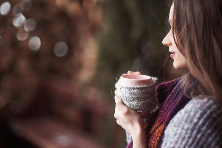 oman wearing warm knit clothes drinking cup of hot tea or coffee outdoors.