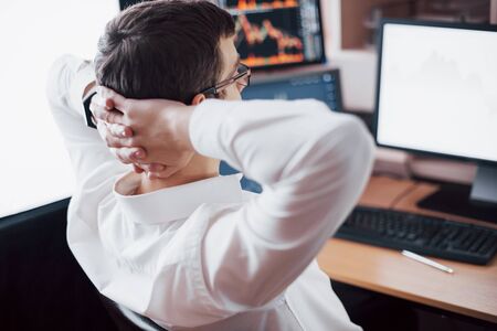 Developing new approaches. Rear view of young man in casual wear holding hand on the back of the head and working while sitting at the desk in creative office.の写真素材