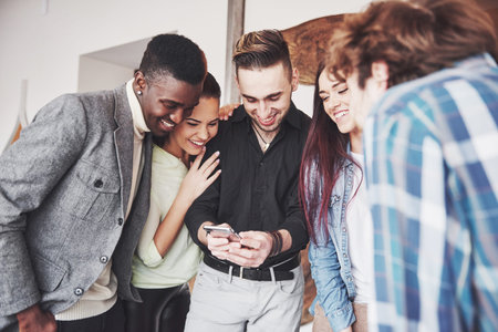 Portrait of cheerful young friends looking at smart phone while sitting in cafe. Mixed race people...