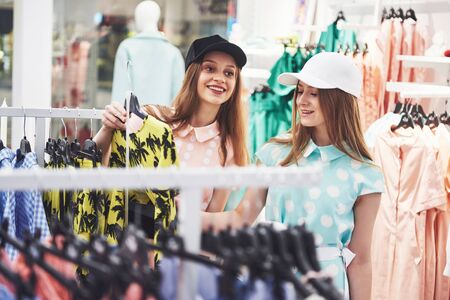 We should look at new dresses Rear view of two beautiful women with shopping bags looking away with smile while walking at the clothing store.の写真素材