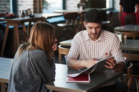 Making some corrections. People have conversation in the restaurant. Man in shirt with stripes speaks to a girl.の写真素材