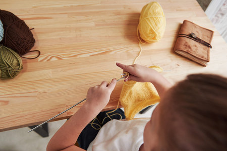 Close up view. Kid is knitting at home. Cute little girl sitting near the wooden table is learning some new stuff.の写真素材