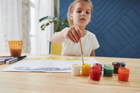Takes the paint. Little girl is drawing by using gouache and brush. Learning in the art class.の写真素材