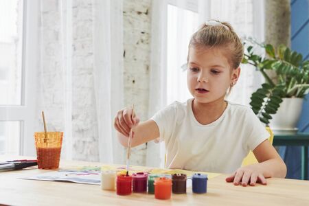 Busy child. Little girl is drawing by using gouache and brush. Learning in the art class.の写真素材