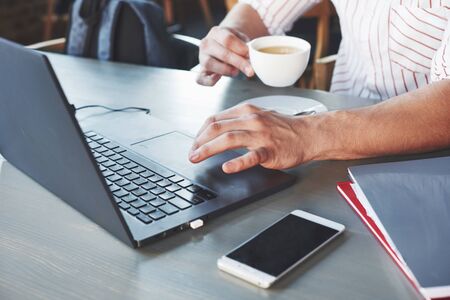 Holds a cup of coffee. Particle view of freelance man working on the project with laptop and notepads on table.の写真素材