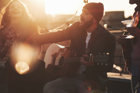 Guy taking something by his hand. Friends have fun at rooftop party with decorative colored light bulbs.の写真素材