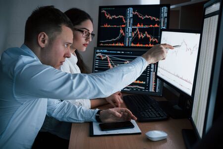 Planning the business project. Team of stockbrokers are having a conversation in a office with multiple display screens.の写真素材