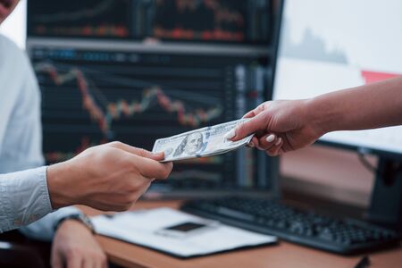 Process of giving and receiving money. Day of salary in the modern office with screens with graphs on them.の写真素材