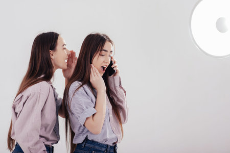 Girl having call and her friend tells what to say. Two sisters twins standing and posing in the...