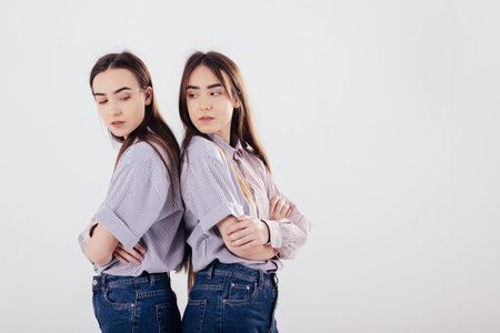 Conception of two offended family members. Two sisters twins standing and posing in the studio with white background.の写真素材