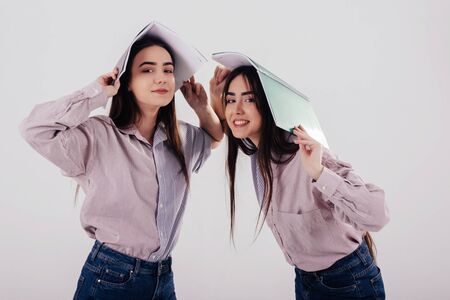 Just having fun with notepads holding on heads. Two sisters twins standing and posing in the studio with white background.の写真素材
