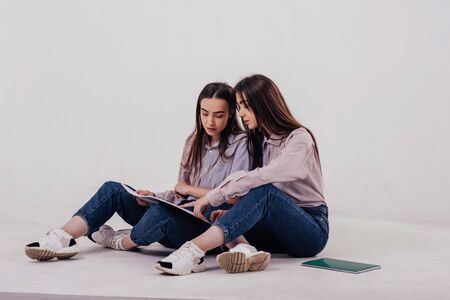 Young students learn new stuff. Two sisters twins sitting and posing in the studio with white background.の写真素材