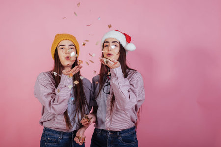 Finally holiday time. Giving air kiss using confetti. Two sisters twins standing and posing in the studio with white background.の写真素材
