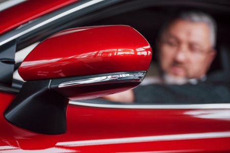 Shiny red vehicle. Side view of senior businessman in official clothes driving a modern new car.の写真素材