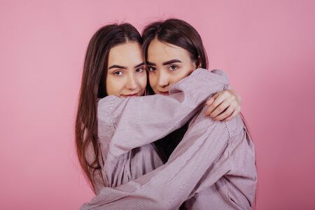 Cute hugs. Two sisters twins standing and posing in the studio with white background.の写真素材