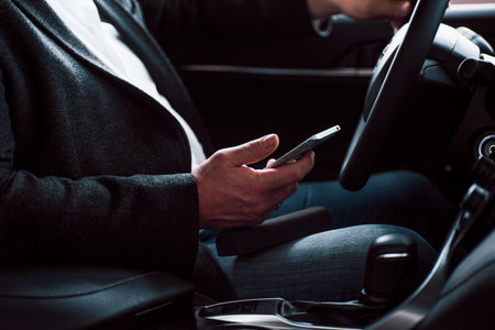 Rich clothes, car and mobile device. Working in the car using silver colored smartphone. Senior...