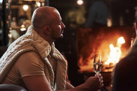 Enjoy the moment. Bald guy with glass of champagne feels satisfaction sitting near the fireplace in the restaurant.の写真素材