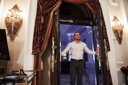 Opening the doors. Modern beautiful guy in official clothes is happy to welcome the visitors.の写真素材