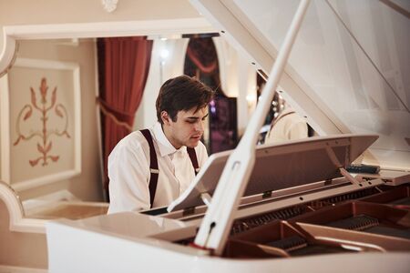 Beautiful man. Young professional musician in official clothes plays on the white piano.の写真素材