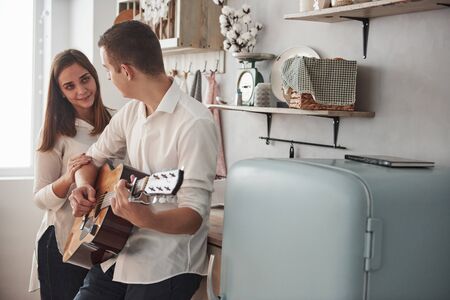 Sweet serenade. Young guitarist playing love song for his girlfriend in the kitchen.の写真素材