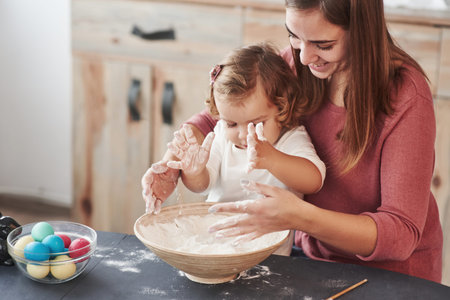 Girl plays with flour. Mother teaches daughter to paint the eggs for the Easter holidays.