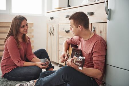 In casual home clothes. Young guitarist playing love song for his girlfriend in the kitchen.の写真素材
