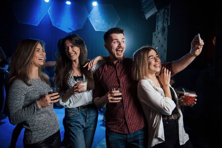 Joking around. Friends taking selfie in beautiful nightclub. With drinks in the hands.の写真素材