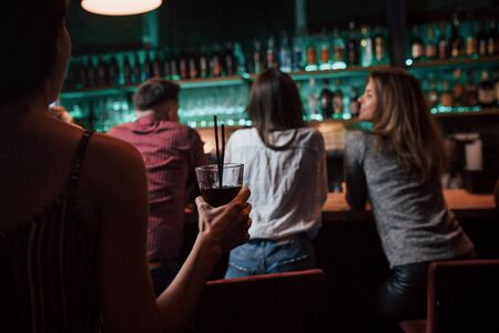 Girl with glass is going to the friends. Beautiful youth have party together with alcohol in the nightclub.の写真素材