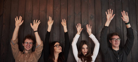 Cropped photo. Celebrating succeess. Friends put their hands up gainst black wooden wall.