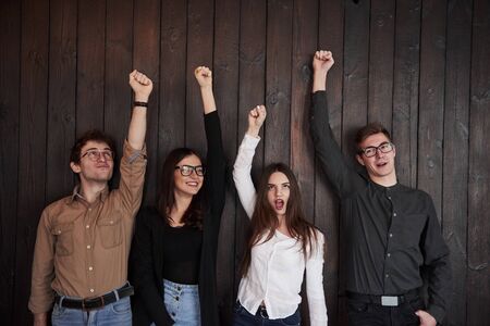 Girl in white shirt screaming. Celebrating succeess. Friends put their hands up against black wooden wall.の写真素材