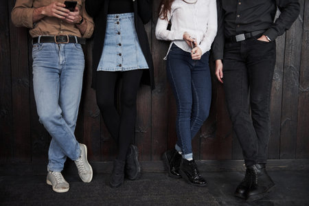 Cropped photo. Youth stands against black wooden wall. Group of friends spending time together.