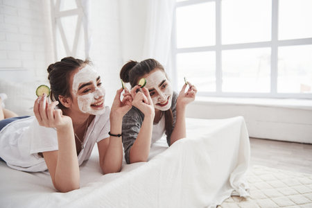 Posing for the cameramen. Conception of skin care by using white mask and cucumbers on the face. Two...