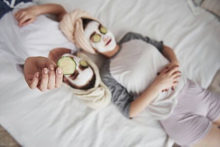 Secret of womans beauty. Lying on the white bed. Top view. Conception of skin care by using white mask and cucumbers on the face.の写真素材