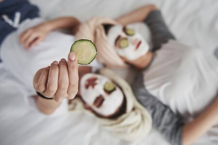 Detailed view. Girl holds cucumber ring in the hand. Lying on the white bed. Conception of skin care.の写真素材
