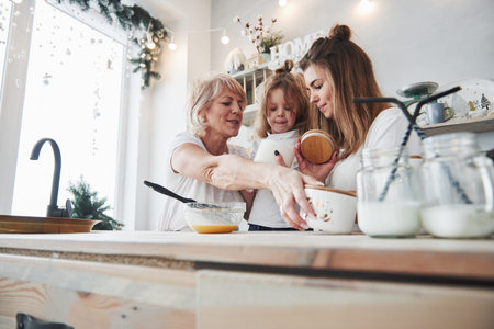 Process of teaching child how to prepare food. Mother, grandmother and daughter having good time in...