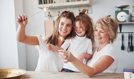 Holiday sparks. Mother, grandmother and daughter having good time in the kitchen.の写真素材